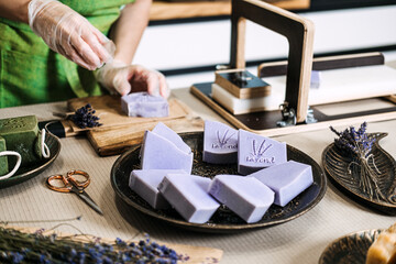 Person stamps lavender soap bar in a home workshop with dried flowers and artisan tools. Sustainable goods, handmade skincare, eco-friendly production, zero waste soap
