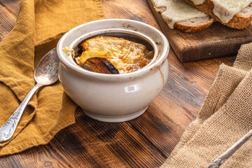 Onion soup in a pot according to a traditional French recipe with a cheese crust, on a wooden background with toasted bread and cheese.