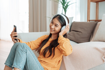 Asian woman listening to music with headphones and mobile phone in living room at home. Headset and sound with song, radio, podcast for motivation and smile