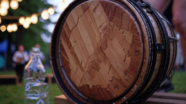Wooden barrel competing in festival rolling contest, blurred spectators and festive string lights surrounding wooden platform background