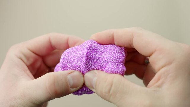 Close-up of fingers squishing purple foam slime in first person view, slow motion
