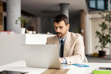 Portrait of executive sitting in office and typing on a laptop.
