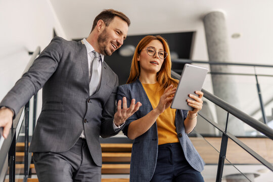 Businesspeople in suit going down the stairs with tablet in hands. - Powered by Adobe
