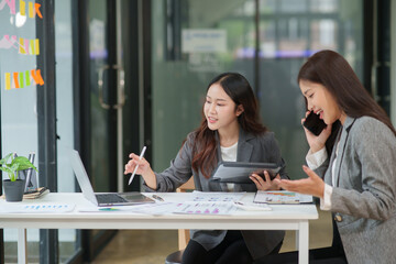 Two Asian businesswomen use calculators to calculate balances and discuss documents and charts in a meeting.
