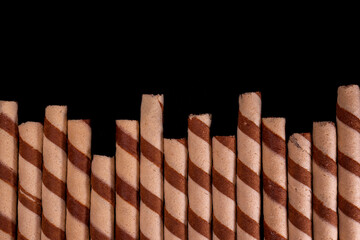 Top view of neatly arranged Chocolate Wafer Rolls with a striped spiral pattern on a dark background. Suitable for advertising and promotion.