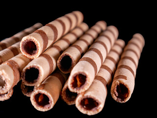 Stack of chocolate wafer sticks with spiral motif neatly arranged on a black background, with studio lighting. Suitable for advertising and promotional designs.