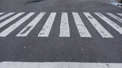 Close-up of a worn pedestrian crossing on an asphalt road, showing urban textures and details of everyday street life. Concept of transportation or city infrastructure.