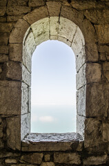 Fototapeta premium Ancient stone arch window frames clear sky view. Rough wall texture contrasts soft light, creating serene, timeless scene. Neutral tones enhance historical ambiance