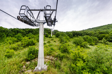 Steel cable car tower stands on verdant mountainside, surrounded by dense trees. Overcast sky...