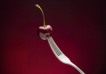 Single ripe cherry on silver fork against deep red background, minimal and elegant food concept