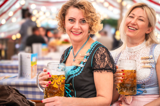 Three friends lift their beer mugs high while celebrating in a lively beer tent. Oktoberfest Munich, G&auml;ubodenvolksfest Straubing, Maidult Regensburg, Germany