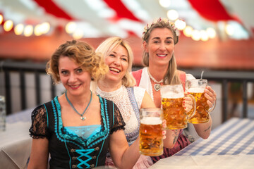 Inside the festive beer tent, friends raise heavy Maß beer mugs in celebration. Oktoberfest...