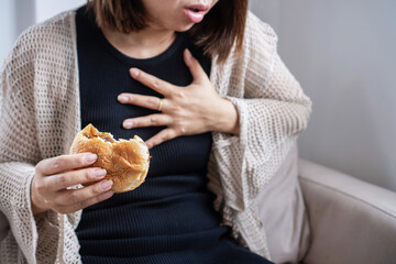 Asian woman experiencing chest pain and trouble swallowing after eating a fast food burger, showing symptoms of acid reflux or GERD (Gastroesophageal Reflux Disease)