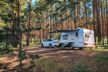 Caravan RV parked on the beach under a trees facing blue sea, lake or river. Family traveling with motorhome. Travelers on an active family vacation.