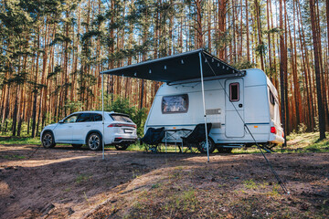 Caravan RV parked on the beach under a trees facing blue sea, lake or river. Family traveling with motorhome. Travelers on an active family vacation.