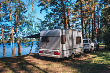 Caravan RV parked on the beach under a trees facing blue sea, lake or river. Family traveling with motorhome. Travelers on an active family vacation.