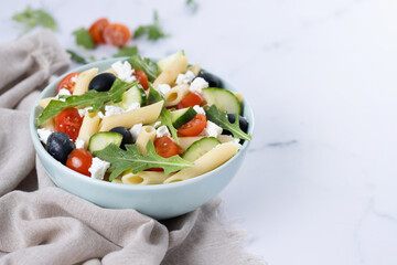 Mediterranean Pasta Salad in bowl with Fresh Vegetables and Herbs on white marble background. Copy space