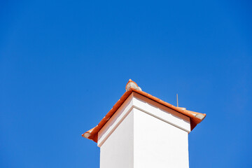 white chimney on a tiled roof in front of a bright blue sky