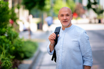 Senior man wearing casual clothes and backpack while walking in downtown