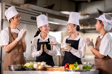 Female chef talking and holding a bowl of peeled onions with students clapping at kitchen counter.