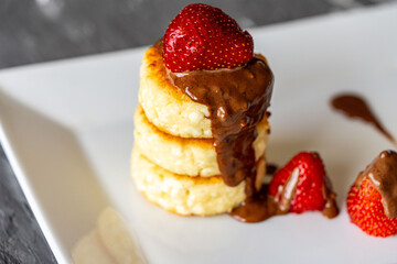 Cottage cheese pancakes or cheesecakes with strawberries and chocolate on a white plate. The concept of a delicious and healthy breakfast. Restaurant serving of the dish. Close-up.
