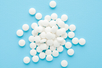 Heap of white pills on light blue table background. Pastel color. Closeup. Top down view.