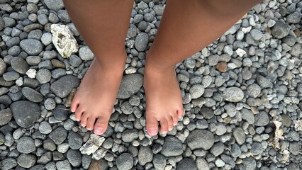 A close-up view shows a child's bare feet standing on a surface covered with numerous grey and brown river stones