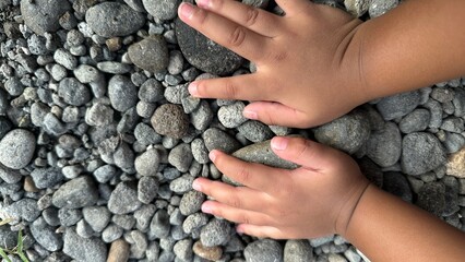 A child's hand gently touches a collection of various-sized grey and brown river rocks