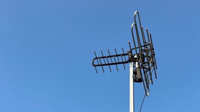 A television antenna, with multiple metallic elements, stands prominently against a clear blue sky