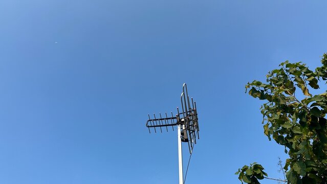 A television antenna, with multiple metallic elements, stands prominently against a clear blue sky