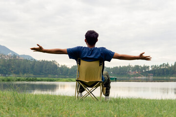 A young man sitting on a chair at lake with relaxing mood, lonely man, Asian man travel alone.