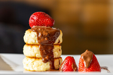 Cottage cheese pancakes or cheesecakes with strawberries and chocolate on a white plate. The concept of a delicious and healthy breakfast. Restaurant serving of the dish. Close-up.