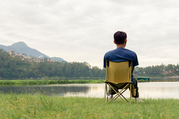 A young man sitting on a chair at lake with relaxing mood, lonely man, Asian man travel alone.