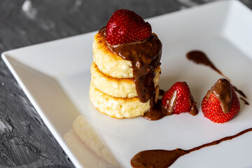 Cottage cheese pancakes or cheesecakes with strawberries and chocolate on a white plate. The concept of a delicious and healthy breakfast. Restaurant serving of the dish. Close-up.