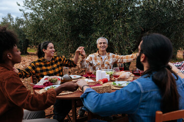 Farmers holding hands during an outdoor meal in olive grove