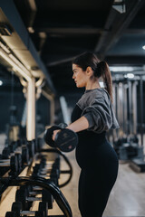 Fototapeta premium A pregnant woman lifts a dumbbell at a gym, emphasizing her commitment to health and fitness during pregnancy. The atmosphere highlights determination and personal care.