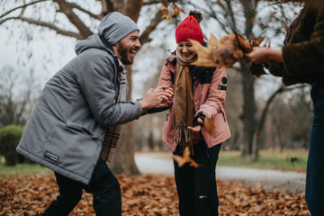 A group of friends enjoying a playful moment with fallen leaves in a park. Their cheerful...