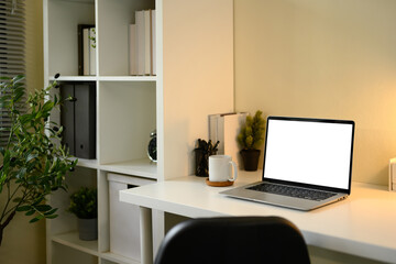 Minimalist home office setup with blank laptop screen, coffee mug, and organized shelf