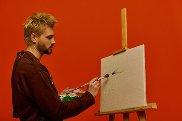 Creative young man paints on canvas against vibrant orange backdrop in artistic expression