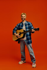 Handsome young man playing guitar against a vibrant orange backdrop for a lively atmosphere