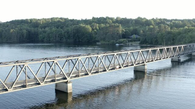 Aerial view flying towards Pont de Lantourne, historic metal truss bridge over lake, Marcillac La Croisille, France