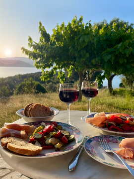 mediterranean dinner outdoor with a view to the garden and the sea in sunset with red wine