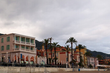 Obraz premium The pastel-coloured skyline of Menton glows at sunset, with charming rooftops and coastal silhouettes. A golden hour view of this French Riviera gem.
