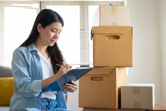 Asian woman checking and packing the carton box prepare to move to new house relocation shipping or check goods package before delivery to customer from online shopping by checklist