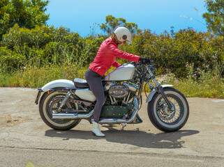 Woman in red leather jacket riding a Harley-Davidson Sportster motorcycle getting ready to ride on...