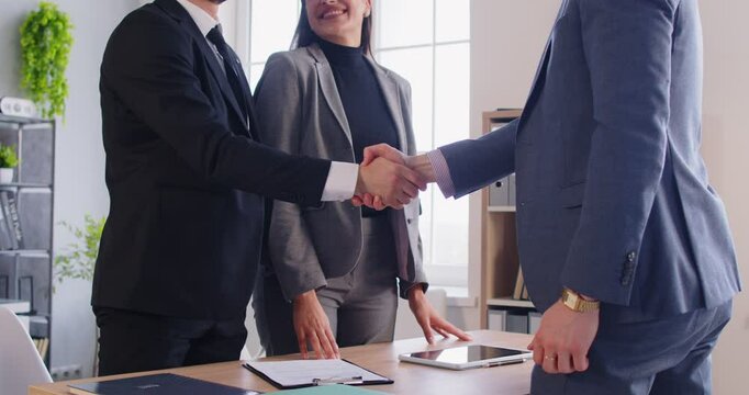 Happy couple shaking hands with business broker or insurance agent. Young man and woman having a good deal signing a contract with their investment adviser in office. 4k video. Slow motion.