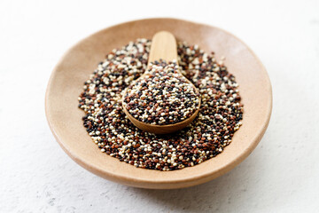 Mix of white, black and red quinoa seeds in wooden spoon.