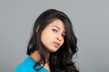 Fototapeta premium A young woman confidently poses wearing blue t-shirt, distressed denim jeans, heels, showcasing a casual urban style with charm and elegance, suitable for haircare, freedom, self-expression project