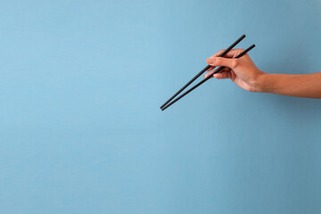 Young Female Hand Holding Black Chopsticks Against Blue Background
