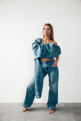 Woman poses stylishly in denim outfit against a minimalistic white background